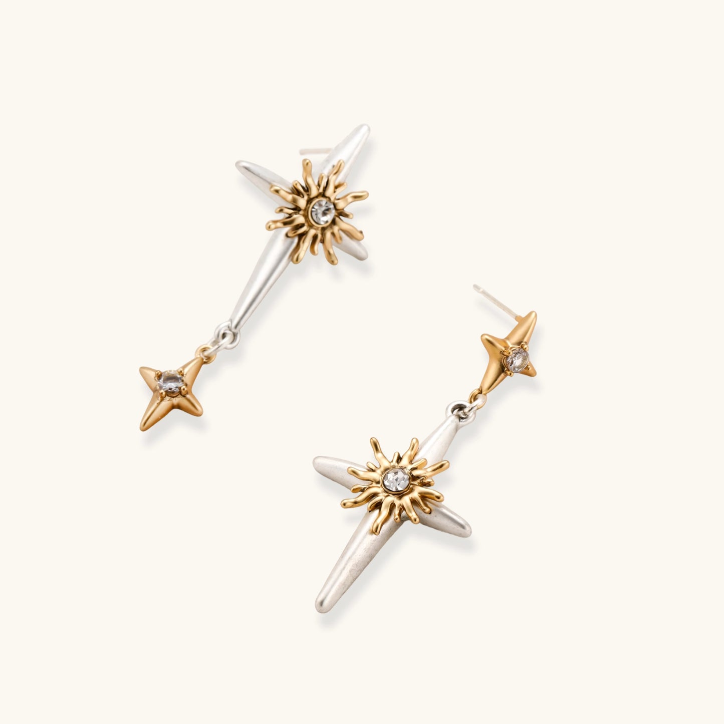 Dangle earrings with silver hoops, gold sun charms with crystals, and gold four-pointed star drops on cream background.