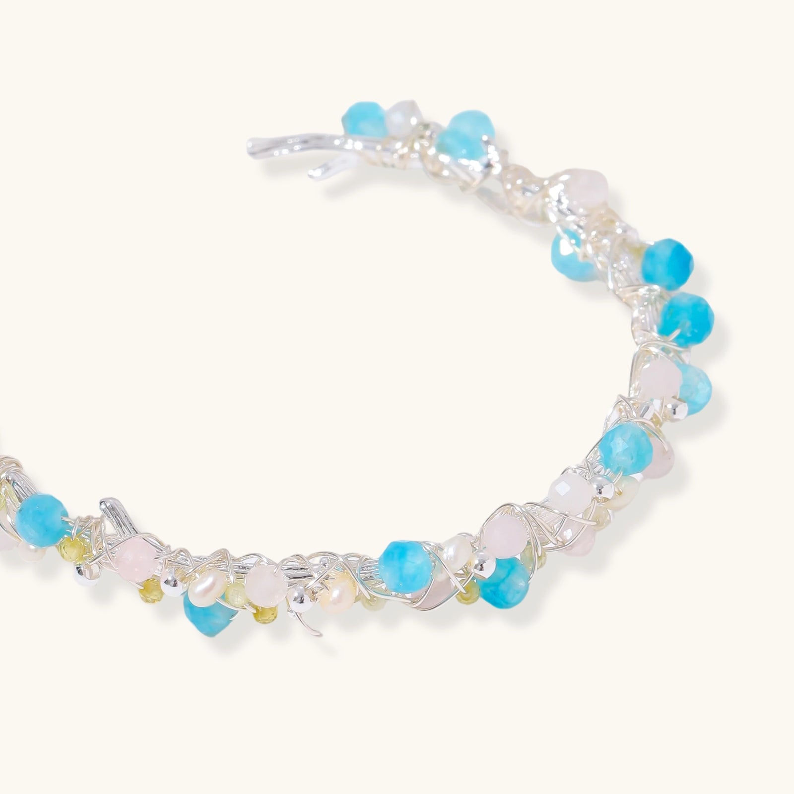 Delicate wire-wrapped bracelet featuring turquoise, rose quartz, freshwater pearls, and zircon on a white background.