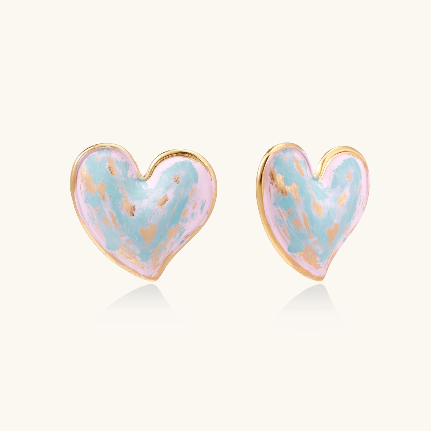 Heart-shaped stud earrings with swirled turquoise and pink enamel in gold-plated frames on cream background
