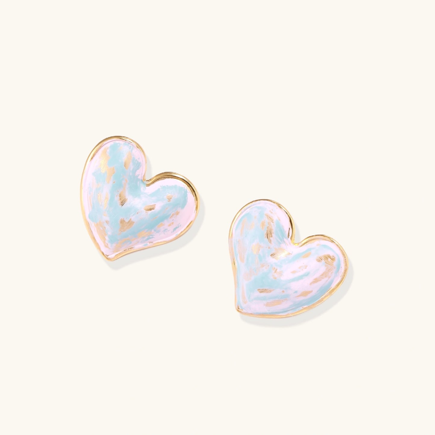 Heart-shaped stud earrings with swirled turquoise and pink enamel in gold-plated frames on cream background