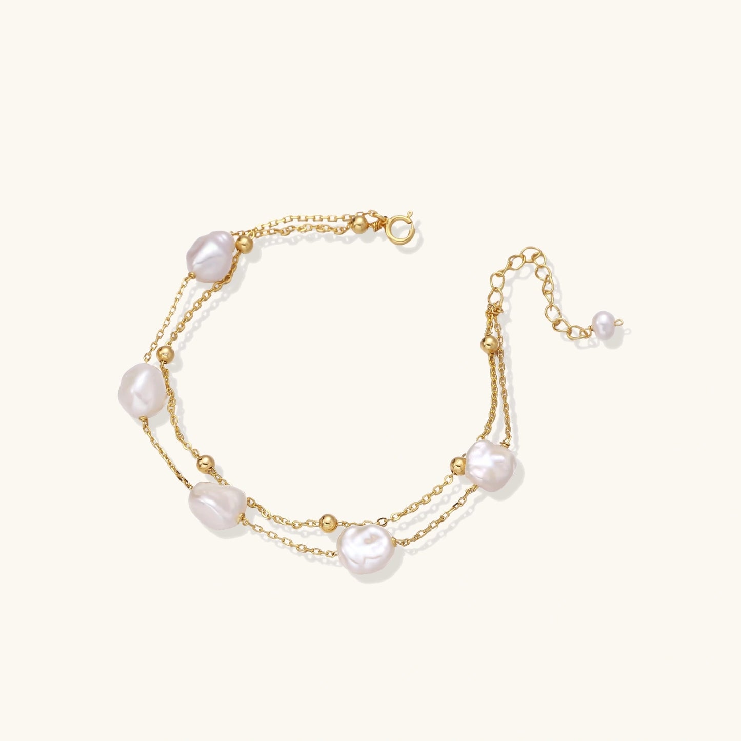 Double-strand gold bracelet with irregular baroque pearls and smooth freshwater pearls on cream background.