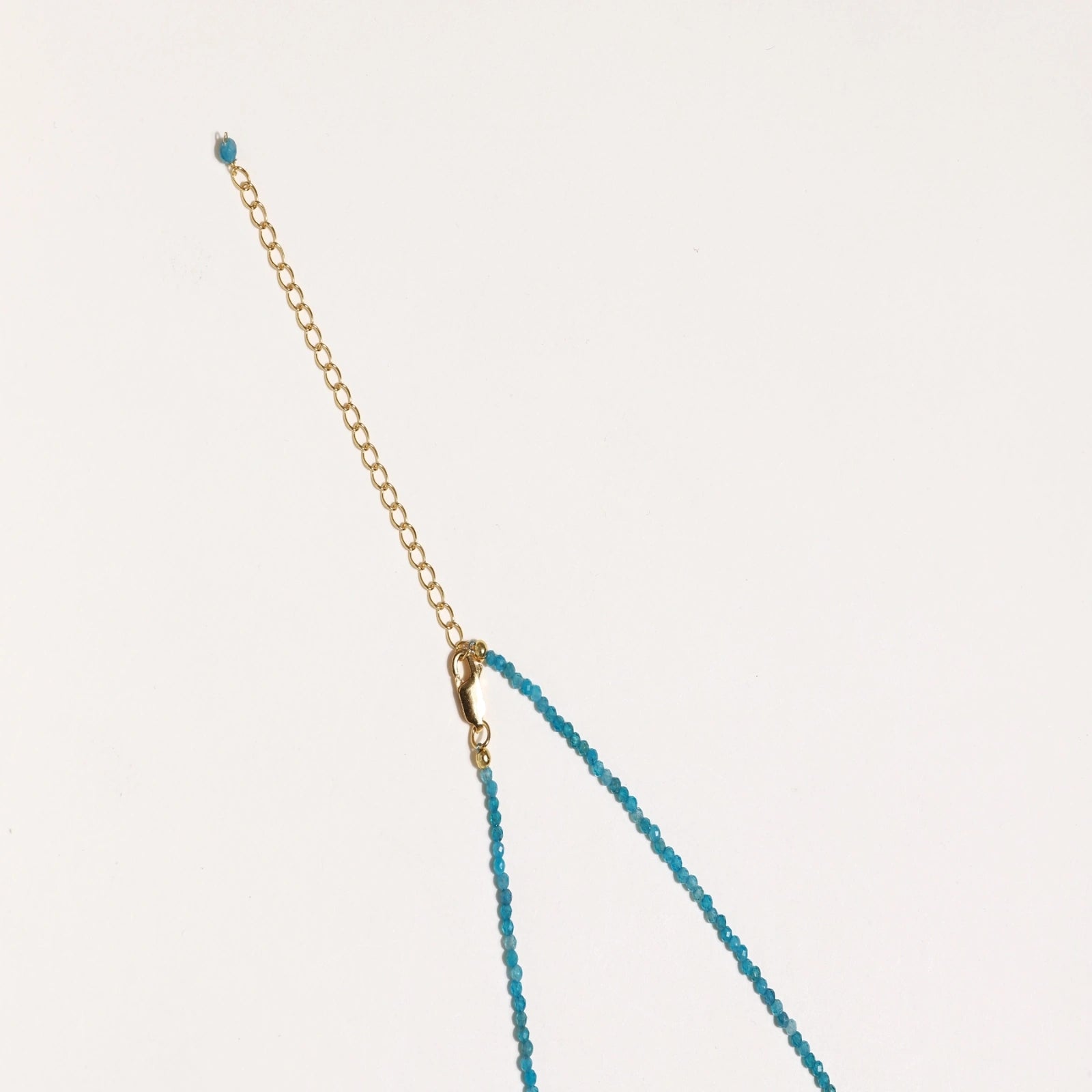 Delicate gold vermeil necklace with teal apatite beads and freshwater pearl on white background.