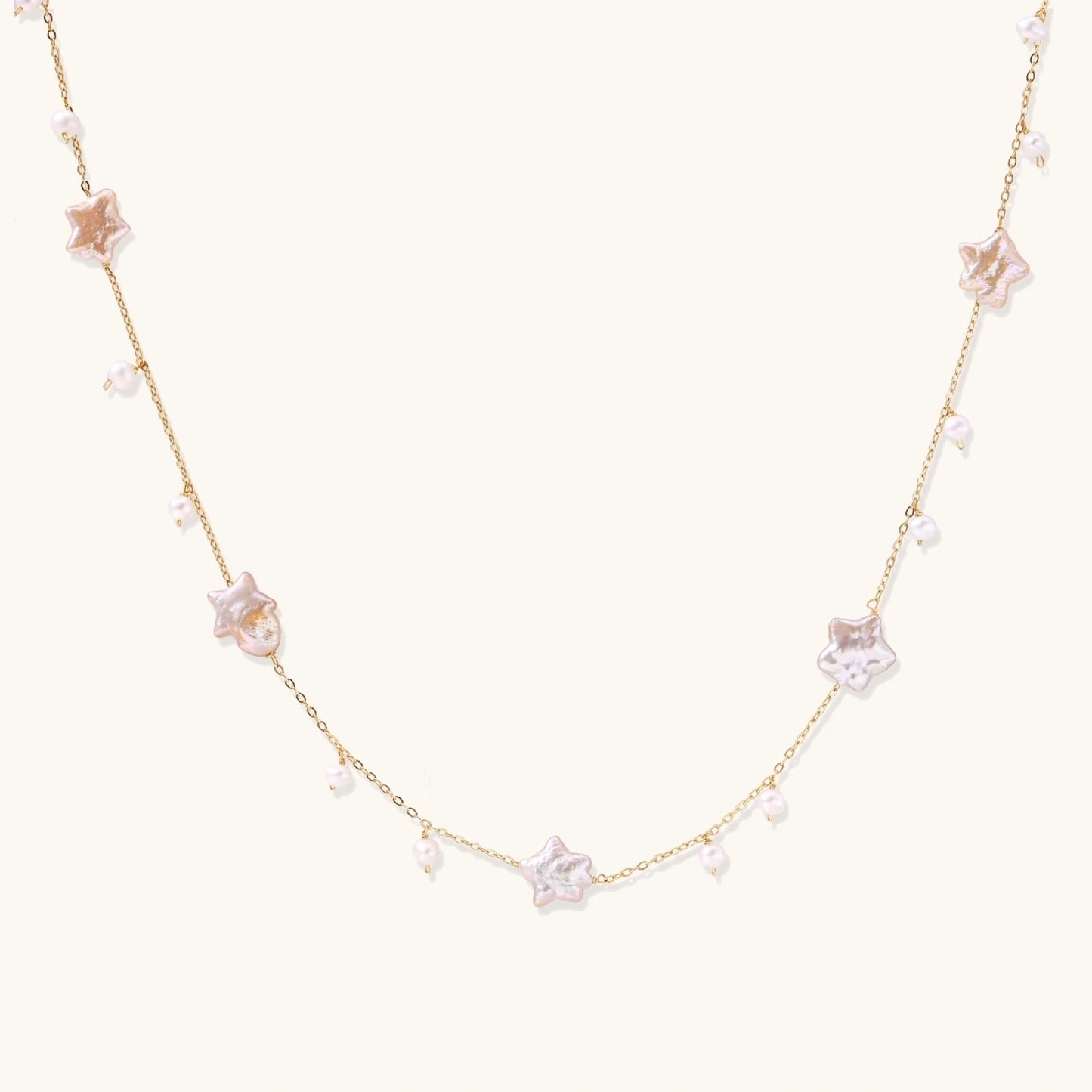 Gold vermeil chain with iridescent star-shaped baroque pearls and small round freshwater pearl drops on cream background.