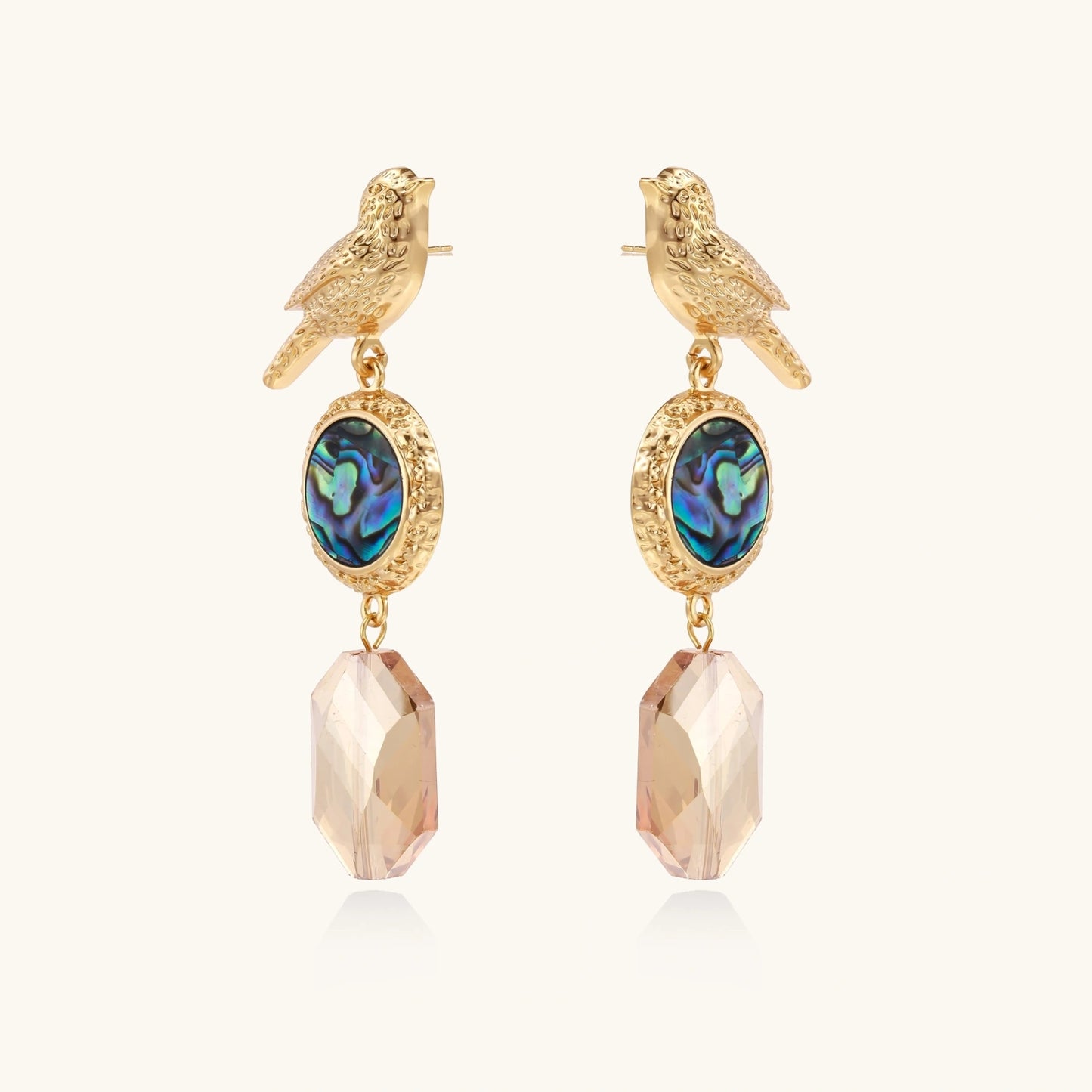 Gold-plated bird stud earrings with iridescent abalone shell medallions and champagne crystal drops on cream background